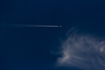 Airplane in the blue sky with white clouds and contrail.