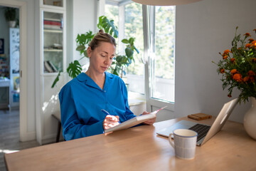 Concentrated pensive woman entrepreneur writing notes in day planner spends productivity morning at home. Thoughtful focused female with diary ponder working tasks, organized to do business remotely.