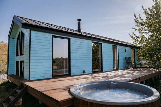 Modern wooden cabin with outdoor hot tub on a sunny deck, ideal for relaxing getaways