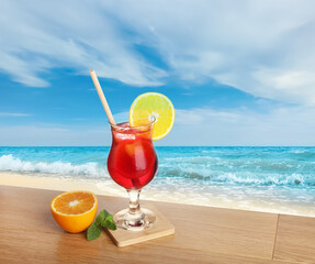 Refreshing drink with straw and fresh orange on wooden table at beach