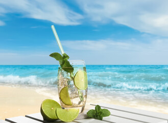 Refreshing drink with straw and fresh lime on wooden table at beach