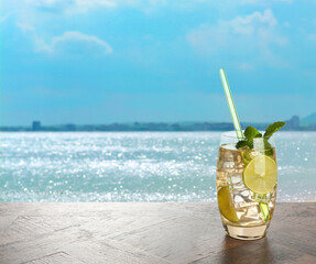 Refreshing drink with straw on wooden table at beach