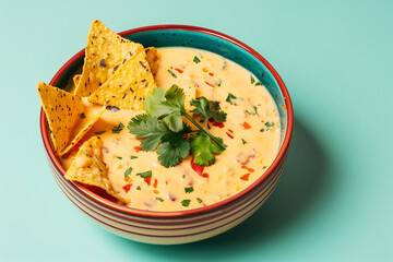 Colorful bowl containing cheesy text queso dip with tortilla chips, garnished with fresh cilantro and ready to be served