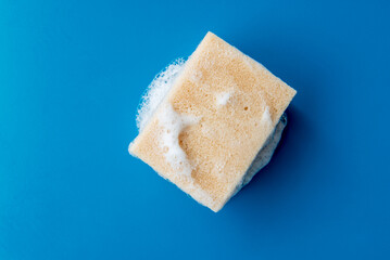 foam sponge for washing dishes on blue ceramic table, copy space.