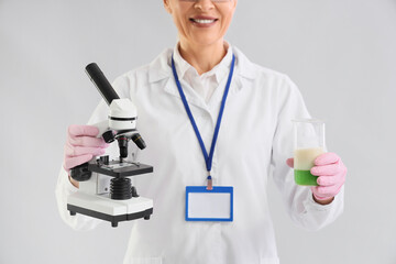 Fototapeta premium Female chemist with microscope and flask on light background, closeup