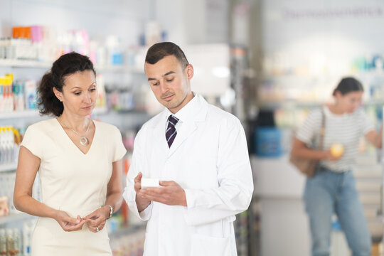 Polite male pharmacist consulting woman customer about medicament in box in chemist's shop