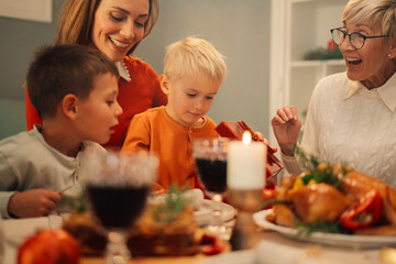 Happy family celebrating christmas opening gifts at dinner table