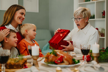 Family having christmas dinner giving gift to surprised grandmother