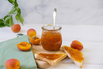 Homemade apricot jam in glass jar on kitchen white background. Summer harvest and canned food. 