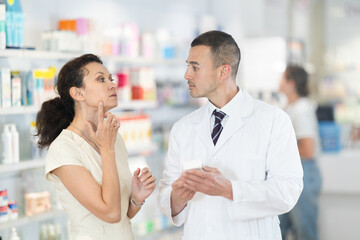 Young male pharmacist advising medicine for toothache to adult woman at pharmacy