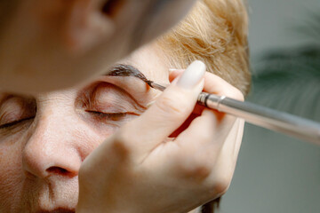 Obraz premium A cosmetologist paints the eyebrows of an elderly woman.