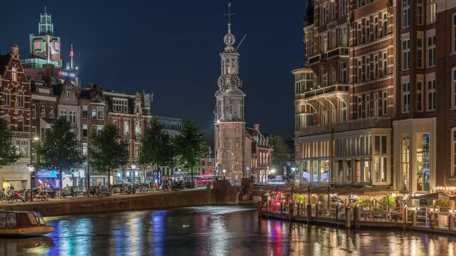 Panoramic timelapse of Amsterdam city center featuring Amstel River, waterfront and Munttoren tower. Boats float back and forth at night. Scenic urban view from bridge. Netherlands