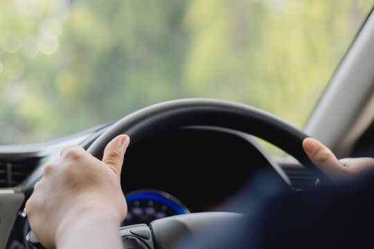 A young man's hand is held on the black steering wheel while he is driving in the car on a highway, a road trip travel concept. Safe Driving, Travel safely.