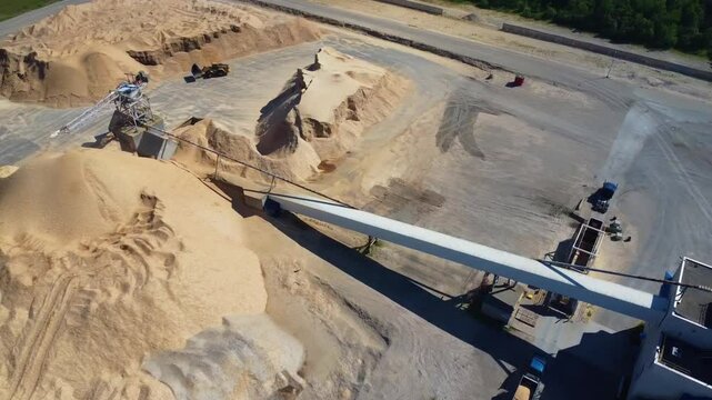 Aerial view of a wood yard with conveyor systems and a bucket loader moving wood chips and waste across large storage piles at an industrial site