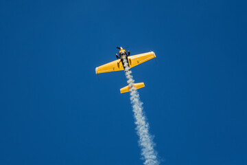 Golden stunt aerobatic plane performing stunts in blue sky with smoke trail. Concept of speed, difficulty, precision, risk