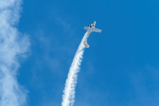 Stunt aerobatic plane performing loop in blue sky with smoke trail. Concept of speed, difficulty, precision, risk, challenge