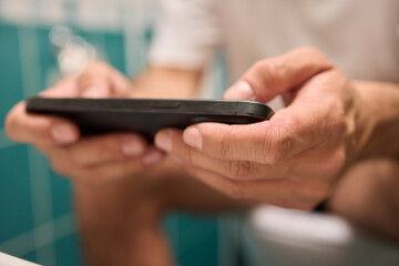 A person casually using their smartphone while seated on the toilet in a modern bathroom