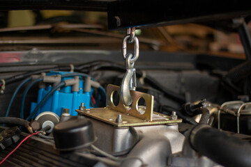 Mechanic working on vehicle engine with specialized lifting equipment in a garage, focusing on repair and restoration tasks