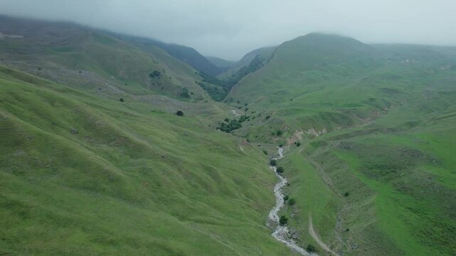 Aerial drone footage showcasing a winding road cutting through the majestic lush green mountains and clouds near Guba, Azerbaijan, Central Asia, Asia