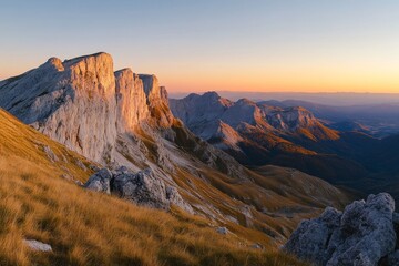 Obraz premium A panoramic view of a mountain range at sunset, with rocky cliffs and golden grass in the foreground.
