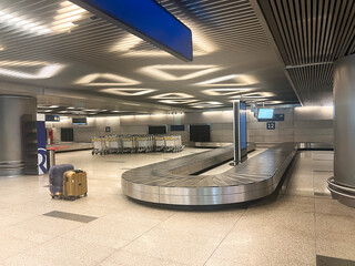 empty airport baggage claim area with two suitcases near the conveyor belt and trolleys in the back