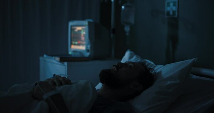 Man lies in hospital bed, eyes open, staring at ceiling.