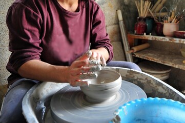 Female potter shaping clay on wheel in home studio.