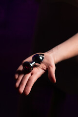 Metal anal plug in hand of sexy girl. Black background. Sex shop, adult store