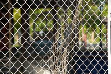A close-up photograph of a chain-link fence. The image focuses on the intertwined metal wires,...