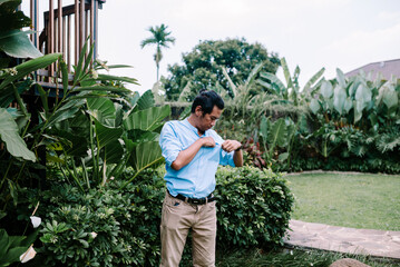 A Southeast Asian man is checking the inside of his shirt pocket, leaning slightly forward to inspect it closely