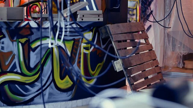 Empty pizza boxes in damaged abandoned warehouse with graffiti drawings on walls. Electric cables hanging in underground location used as crime haven by delinquents, urban background