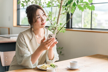カフェでランチをしながらスマホを見る若いアジア人女性
