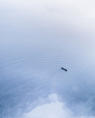A minimalist aerial view of a lone boat on a vast body of water. The boat is positioned in the lower right corner, creating a sense of balance and solitude.