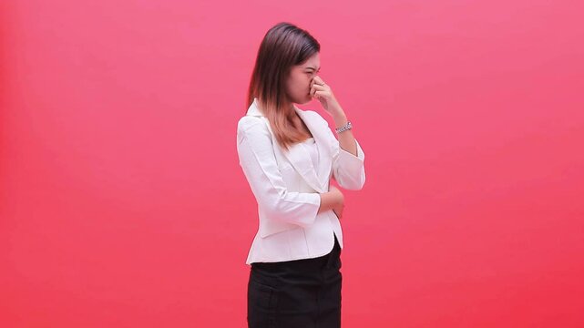 girl wearing a white office suit can't stand the smell of a corpse, holding her nose with her arms crossed, standing on her left side isolated on a red background, for health, science, education