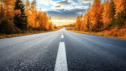 Fototapeta premium A winding road meanders through a valley filled with radiant autumn trees, their golden leaves glistening in the bright sunlight while snow dusts the mountain peaks in the background.