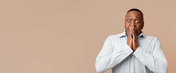 Shocked african american mature man looking at camera, closing mouth in amazement, orange background