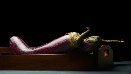 fresh eggplant or aubergine on wooden tray black background, dark purple glossy skin with striped vegetable brinjal on table top, soft focus with dramatic lighting