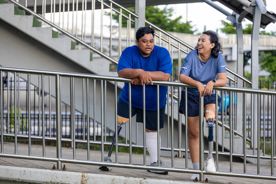 Asian couple with leg amputated are doing walking exercise in urban pathway together for diversity society, inclusive modern infrastructure and accessibility design concept