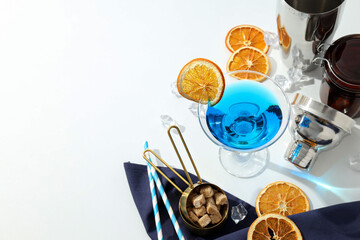 Blue cocktail in glass, orange slices, straws, sugar and tools on white background, space for text