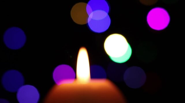 Una toma de cerca de una vela blanca desenfocada rodeado de luces de navidad de varios colores. Imagen de video desenfocada. 
