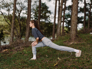 Focused young woman stretching in a forest, preparing for exercise, wearing comfortable sportswear...
