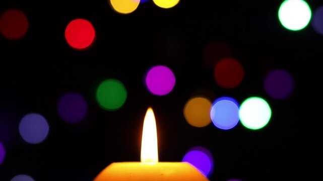 Una toma de cerca de una vela con llama de color blanca rodeada de luces de navidad de varios colores.  Decoraci&oacute;n de navidad y fin de a&ntilde;o