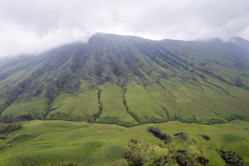 Dramatic aerial view of a volcanic mountain surrounded by lush green hills at Teletubbies Hill, Bromo, Indonesia.