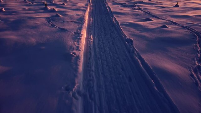 Snowmobile tracks filmed from above slowly tilting up revealing a beautiful field covered in snow infront of a forest during golden hour sunset