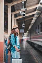 Obraz premium A young woman with a suitcase and backpack waits at a train station, ready for her next travel adventure.