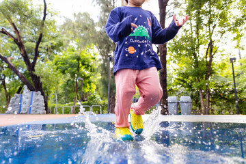 Little preschool 3 year girl enjoying run on water outdoor playground park after rainy day