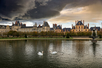 Fototapeta premium Château de Fontainebleau under stormy skies with swans swimming in a calm pond