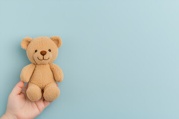 Obraz premium A soft and adorable teddy bear held in a child's hand against a calm blue background perfect for capturing tender moments