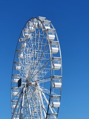 A towering Ferris wheel with white cabins against a vibrant blue sky. Perfect for amusement park, summer fun, and travel themes.