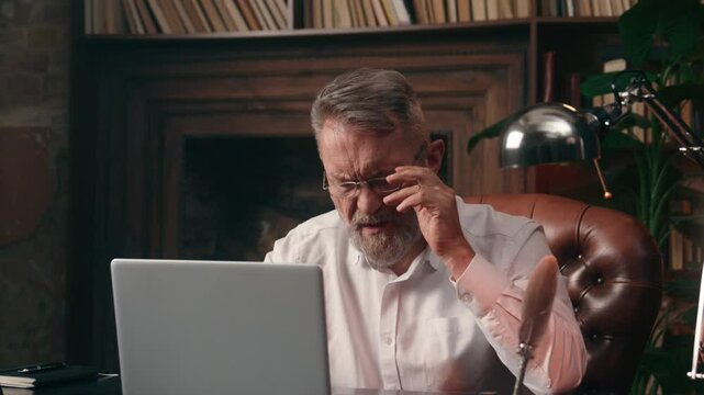 Caucasian old man holding head headache ill unhealthy medicine suffer takes off glasses working laptop businessman business pain computer elderly office male mature technology senior inside migraine